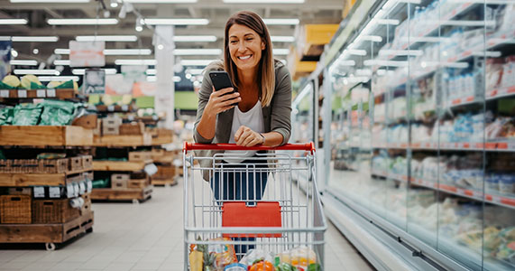 Loyal customer in shopping in grocery store, and using customer loyalty app on smart phone.